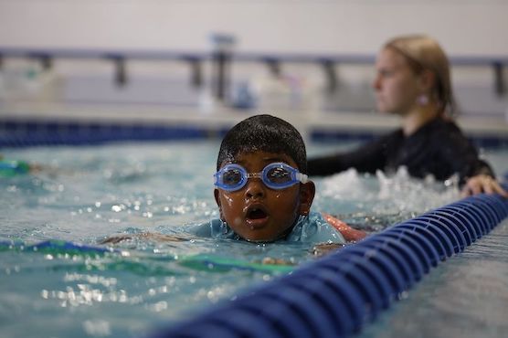 Young boy swimming during a lesson with a pool noodle