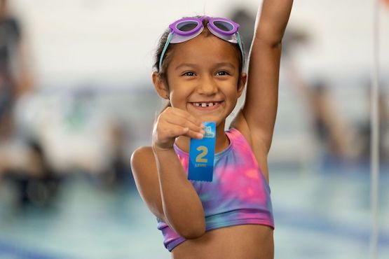 Young girl swimmer proudly showing off her achievement ribbon