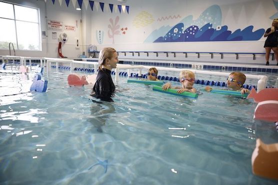 Three young swimmers laughing and smiling together during a swim lesson