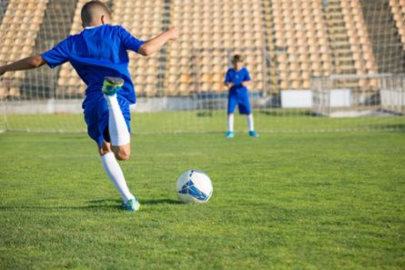 A young boy in a soccer uniform prepares to kick a soccer ball into a goal
