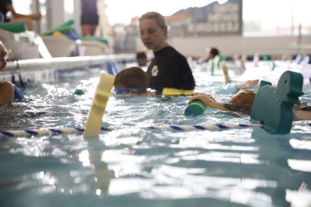 Swimmers practice with a pool noodle during a lesson