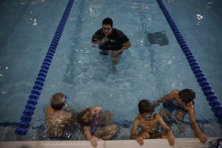 Four young swimmers in a pool follow directions from their instructor