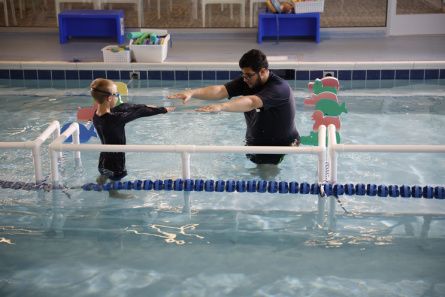 A young swimmer in a pool practices strokes with his swim instructor