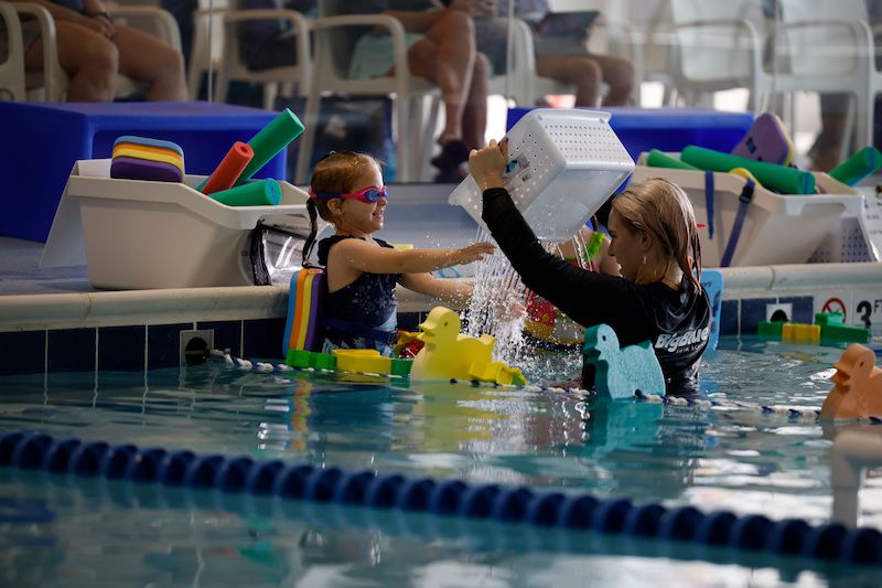 Friendly instructor helping girl build trust and confidence during swimming lessons