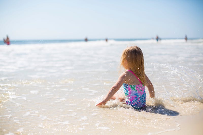 Little girl sitting in the shore enjoying the small waves