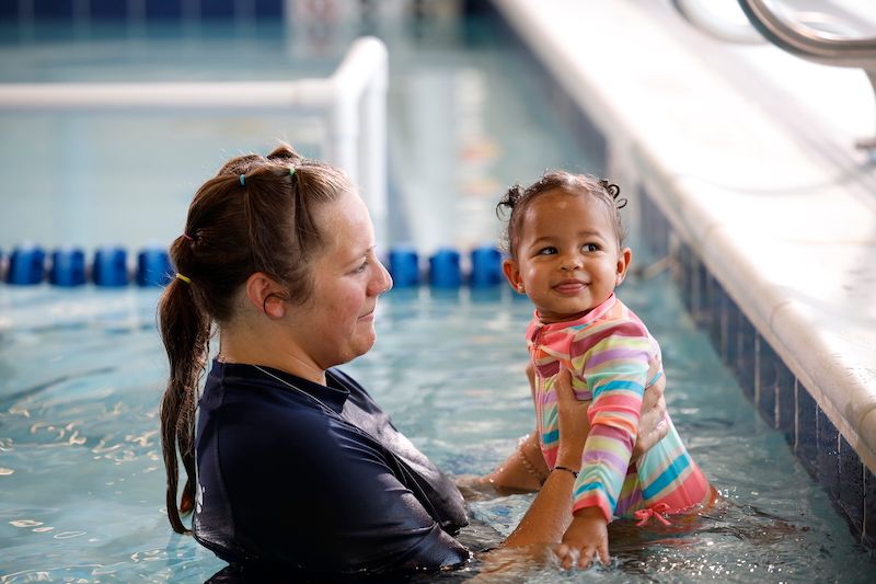 Little baby girl taking swim lessons with a professional instructor