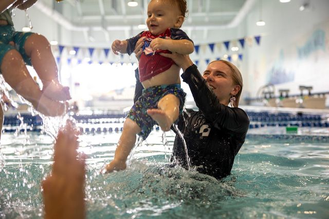 A swim instructor lifts a baby out of the pool