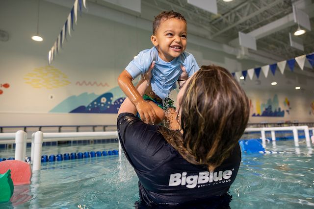 Big Blue swim instructor lifts smiling child out of the water