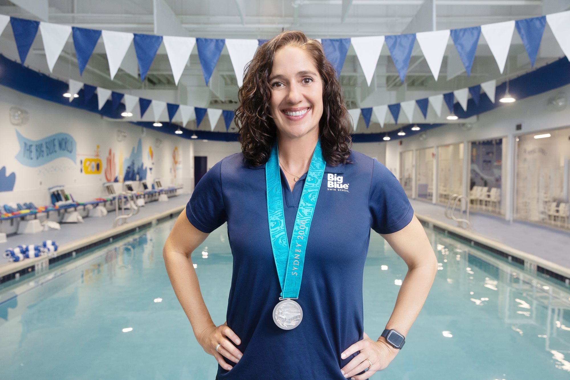 Olympic medalist, Kristy Kowal, stands on a Big Blue pool deck, wearing her silver medal