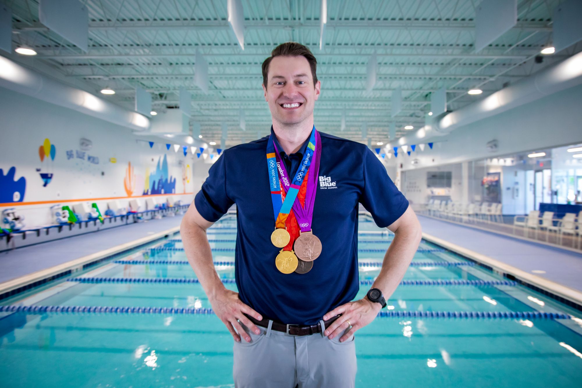 Olympic medalist, Peter Vanderkaay, stands on a Big Blue pool deck, wearing his medals