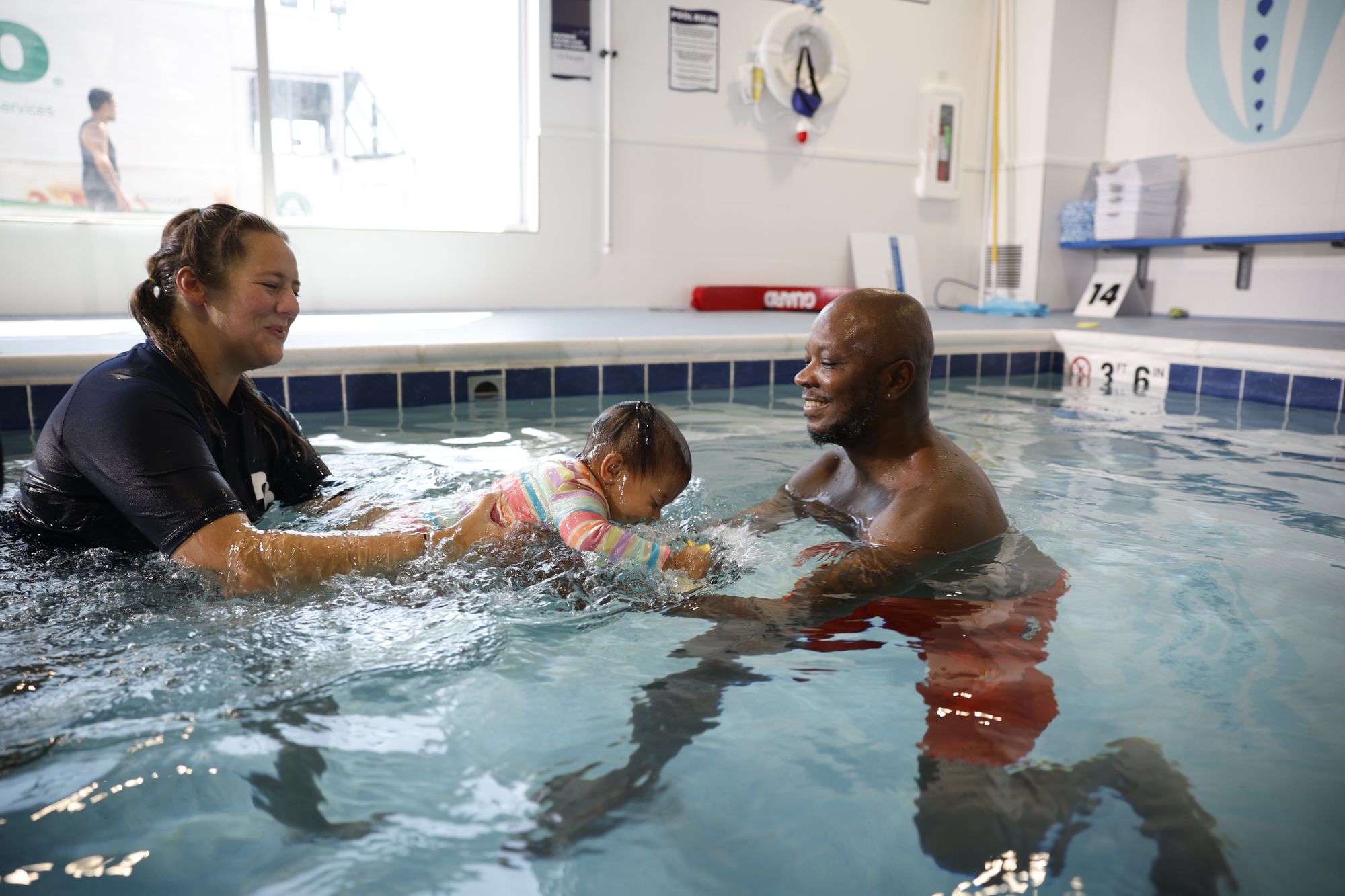 A Big Blue swim instructor helps guide a baby swimmer to her dad during a lesson