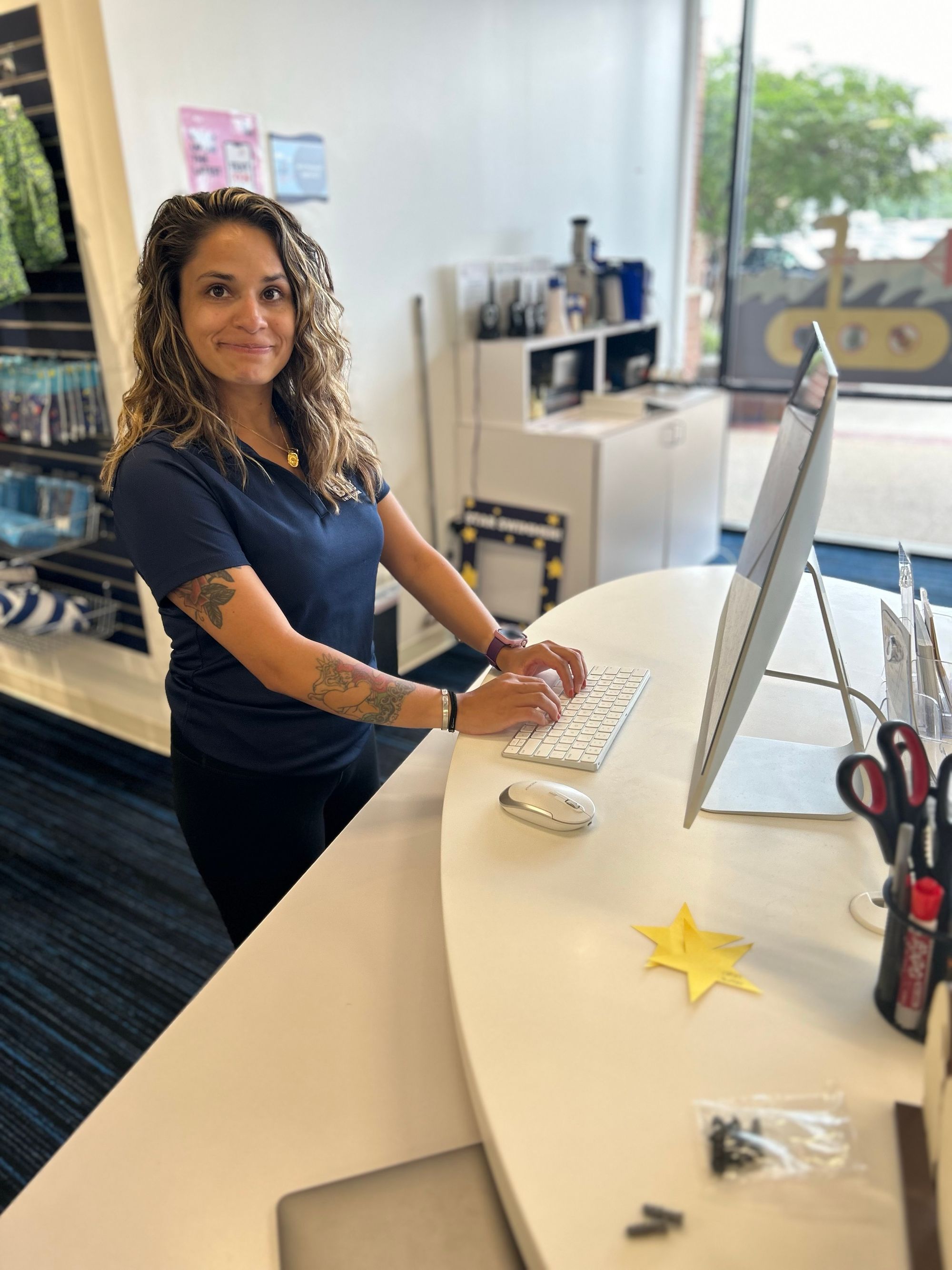 Big Blue staff member, Jessica, stands at the front desk at Big Blue Springfield working on the computer and smiling to to the camera