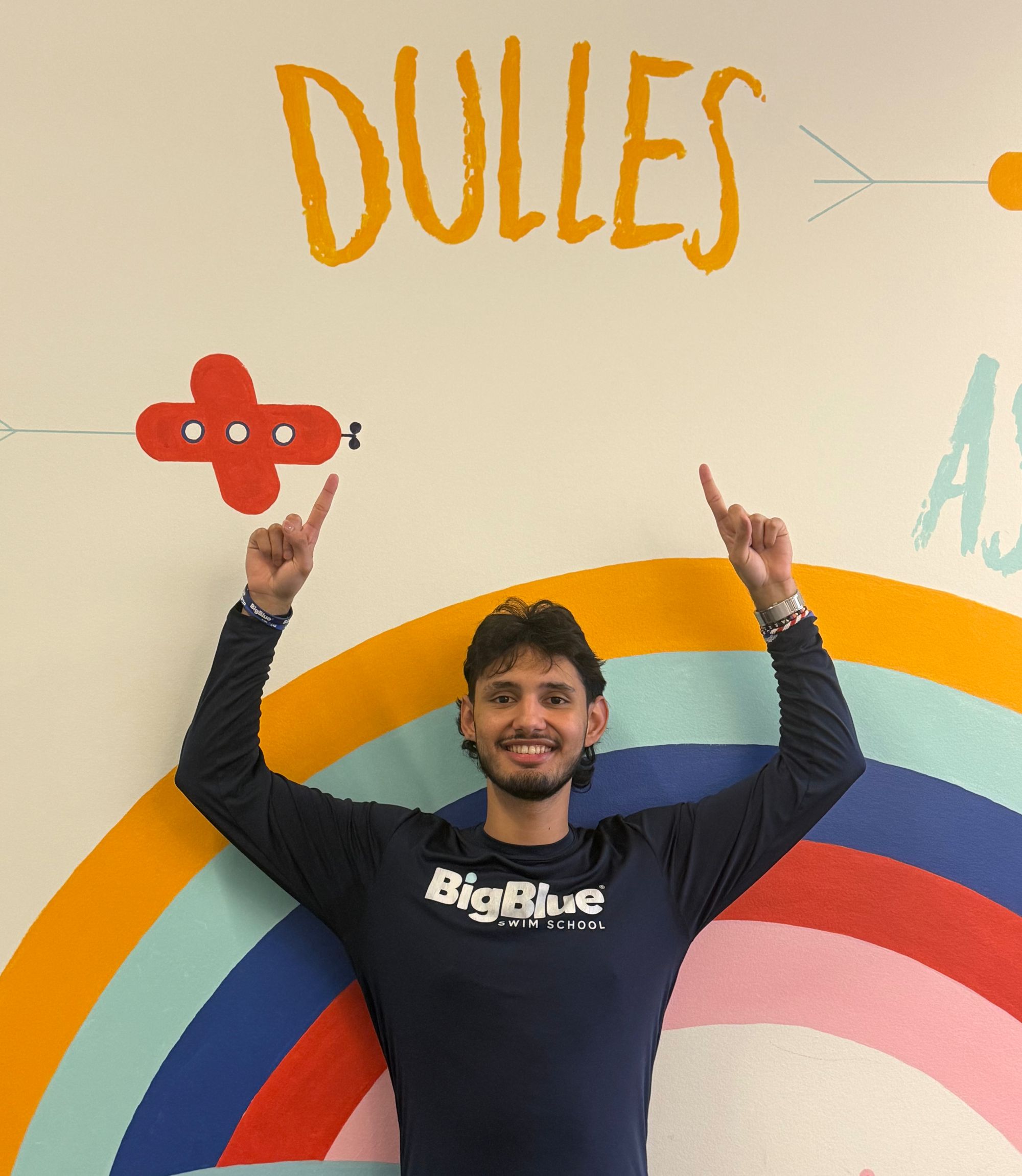 Assistant Manager of Big Blue Dulles, Andres, stands in front of the Dulles mural at the pool.