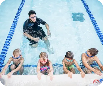 Swim instructor leading a group of four young children holding the pool wall during a kids swim lesson at Big Blue Swim School