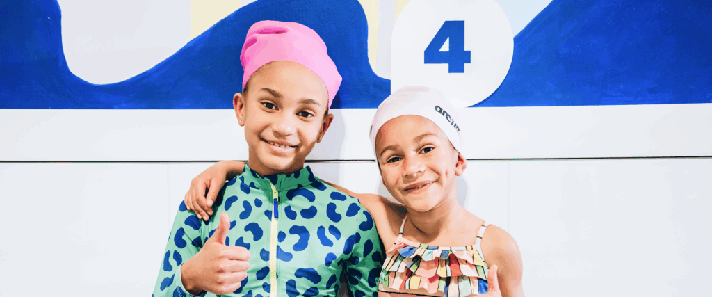 Two young girls smiling at the camera, posing in swim gear.