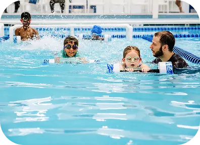 Swim instructor guiding two young children with kick boards during a swim lesson