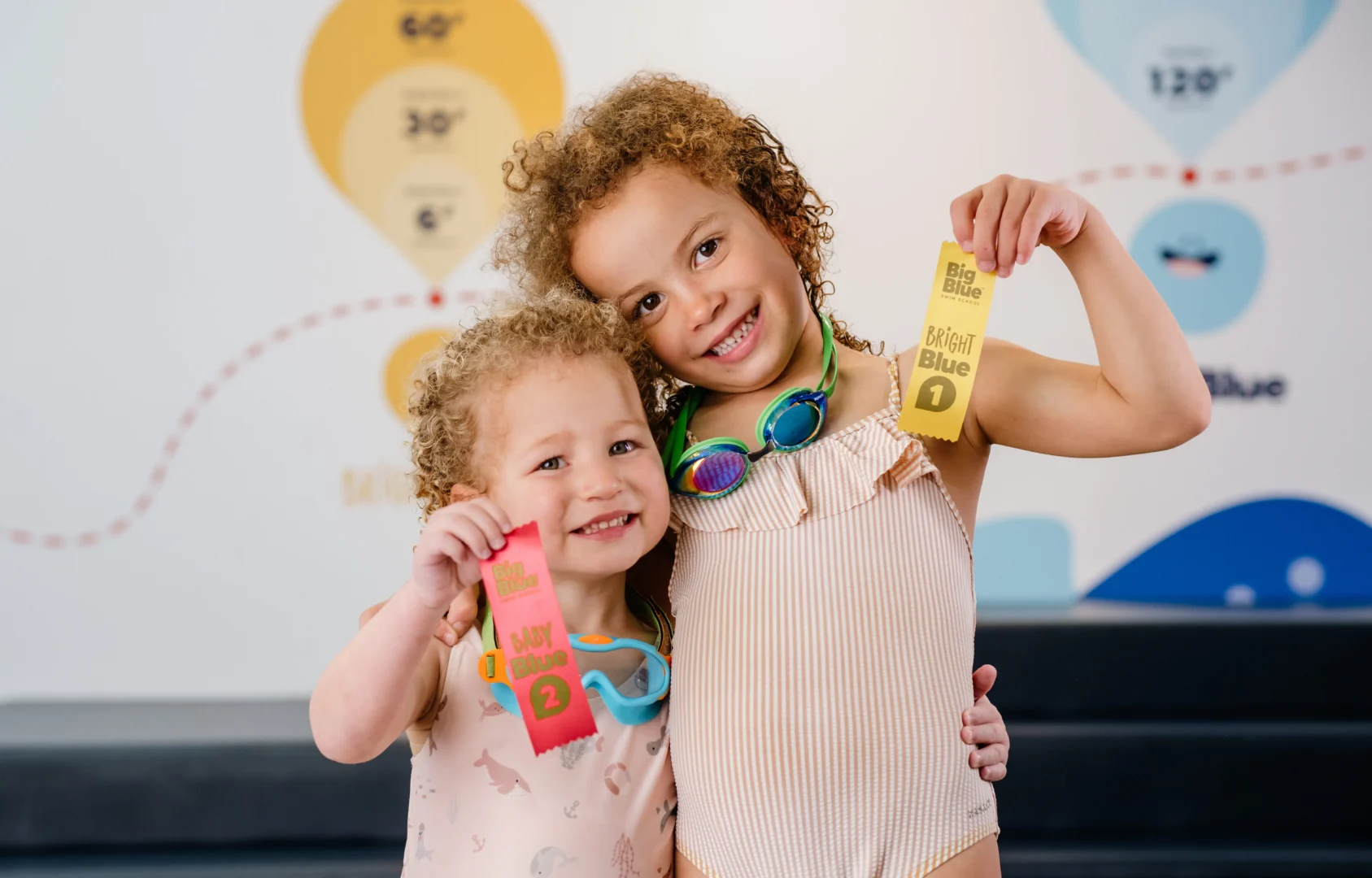 two young girls holding swim ribbons and a Big Blue Swim School medal after class