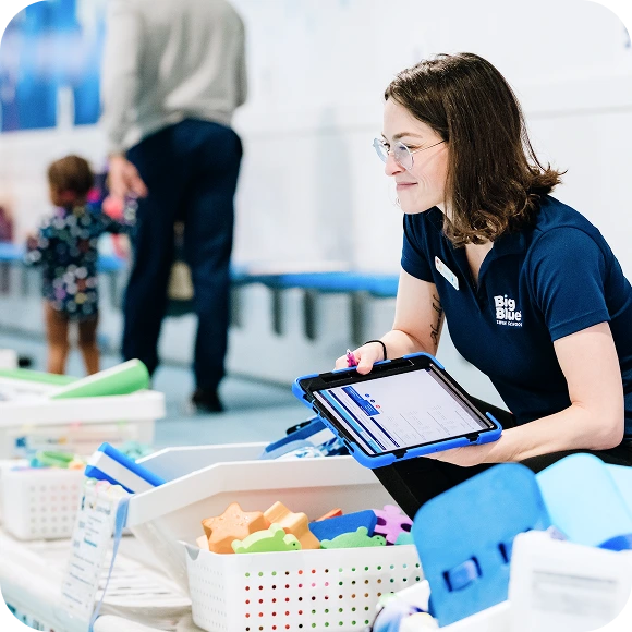 a Big Blue Swim School instructor crouched near a bucket of pool instruction tools